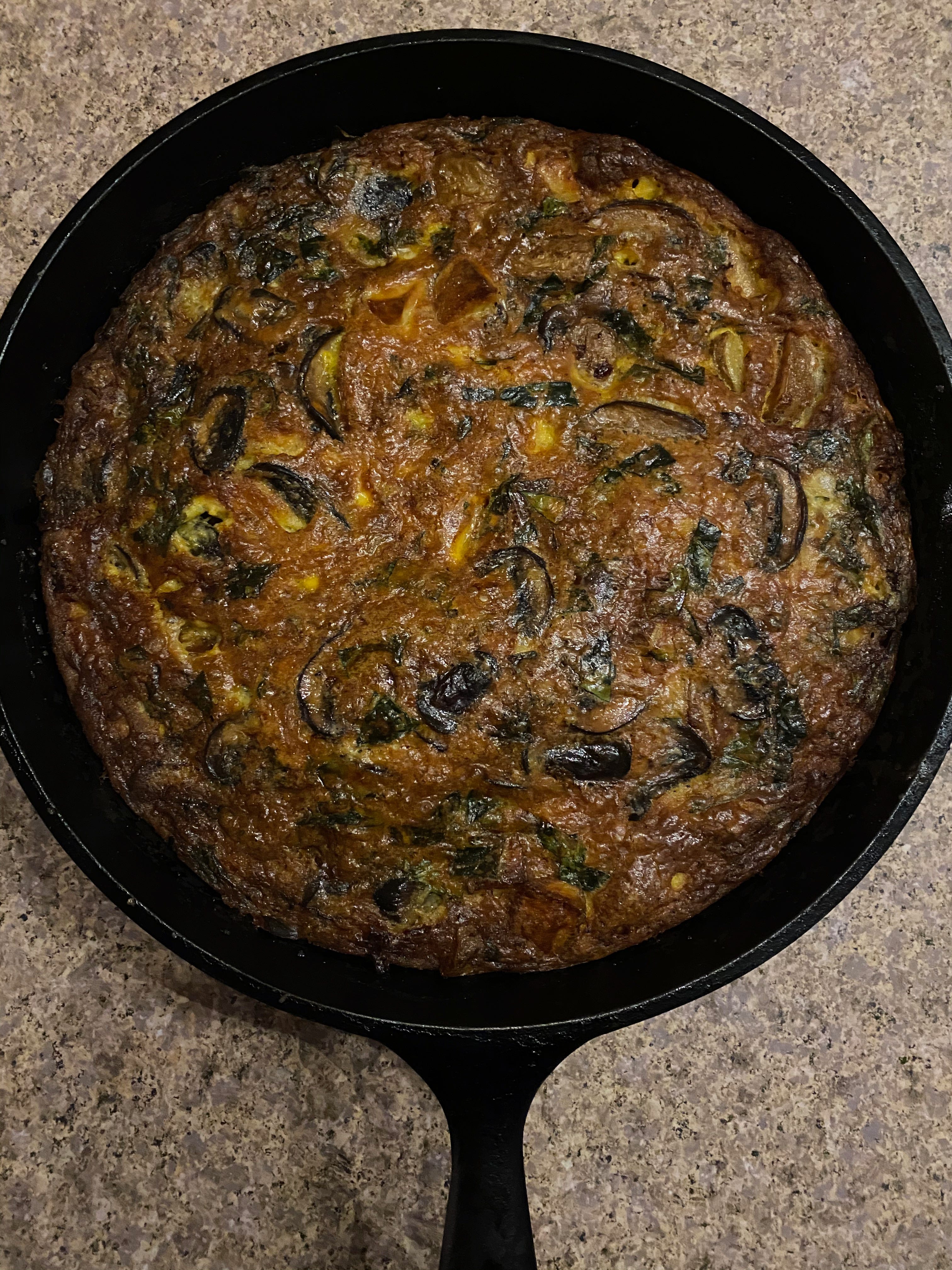 A frittata in a cast-iron pan. It is browned on top and studded with mushrooms.