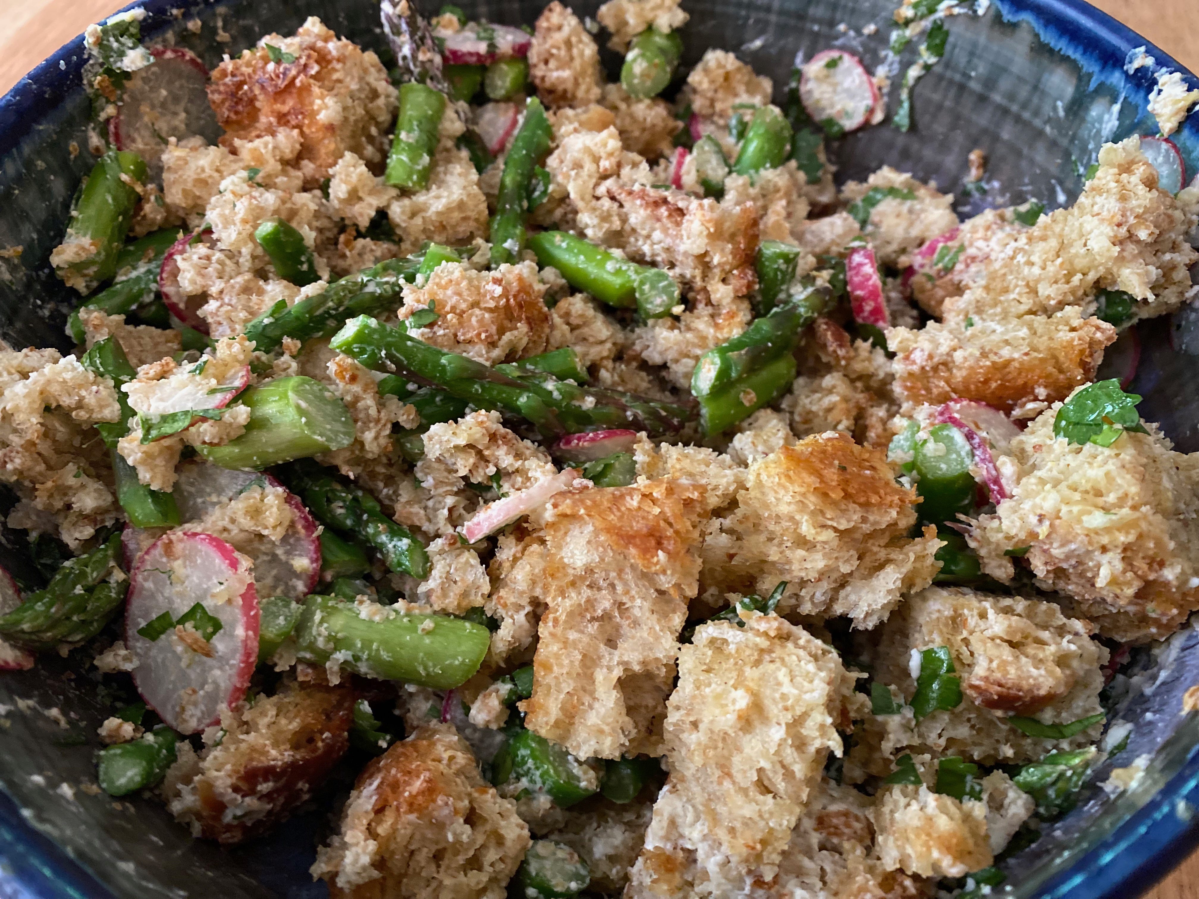 Closeup of a bread, asparagus, and goat cheese salad in a blue ceramic bowl.