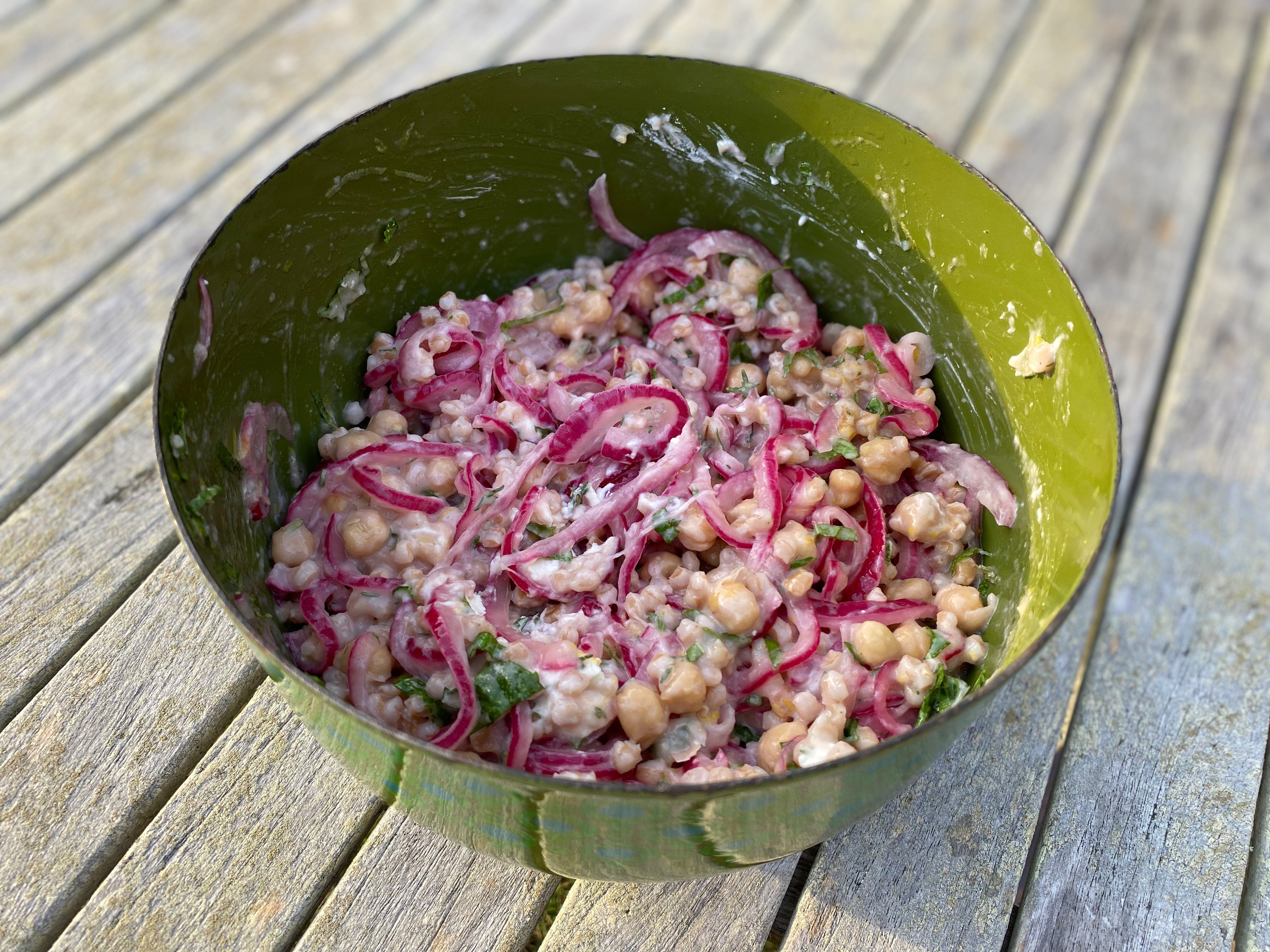 A green bowl of farro salad topped with lots of pickled red onions.