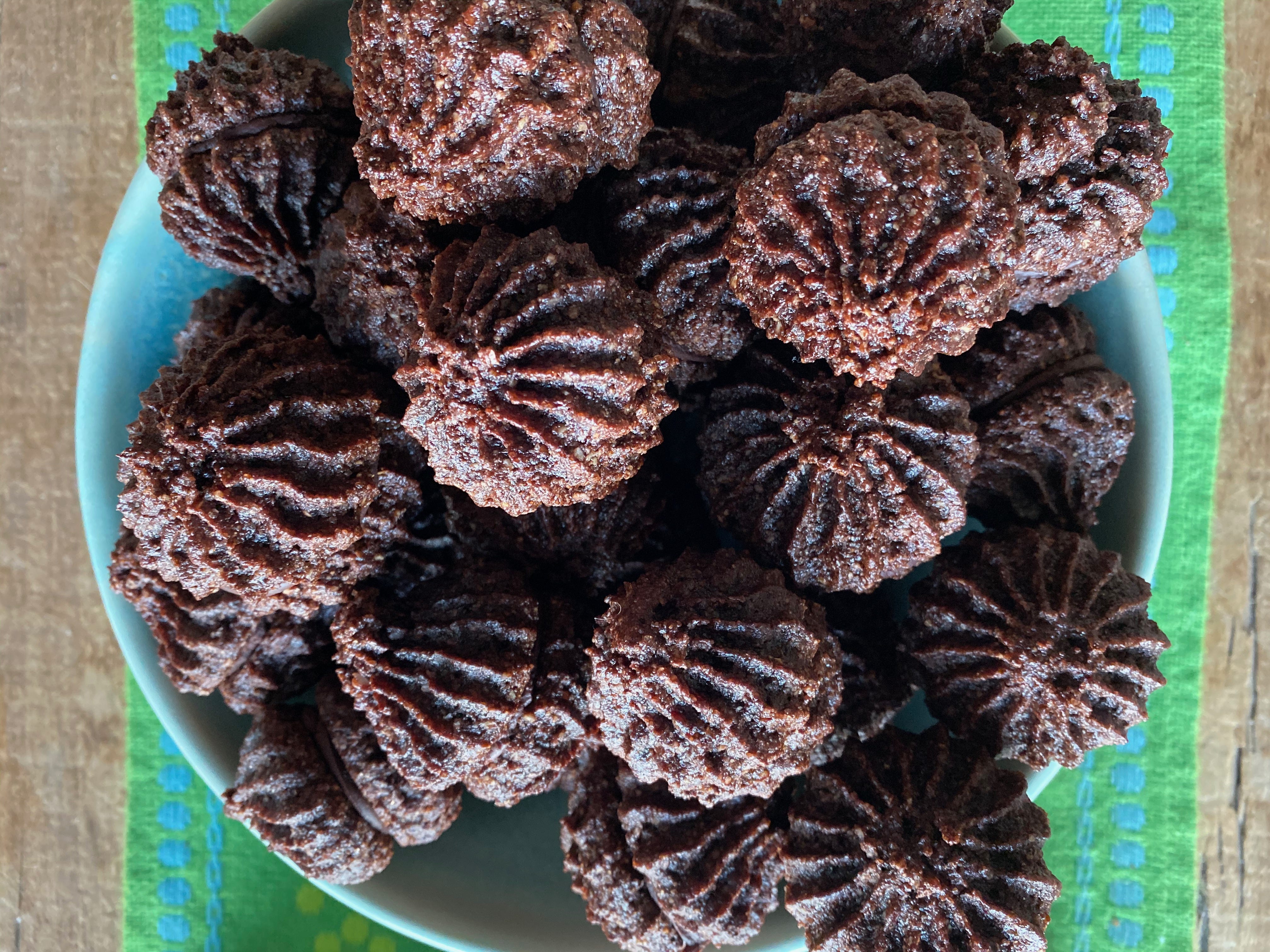 A blue ceramic bowl overflowing with small chocolate cookies. They are shaped like teardrops. The outsides have little ridges from a fluted piping bag, and each cookie is sandwiched with a little bit of chocolate.