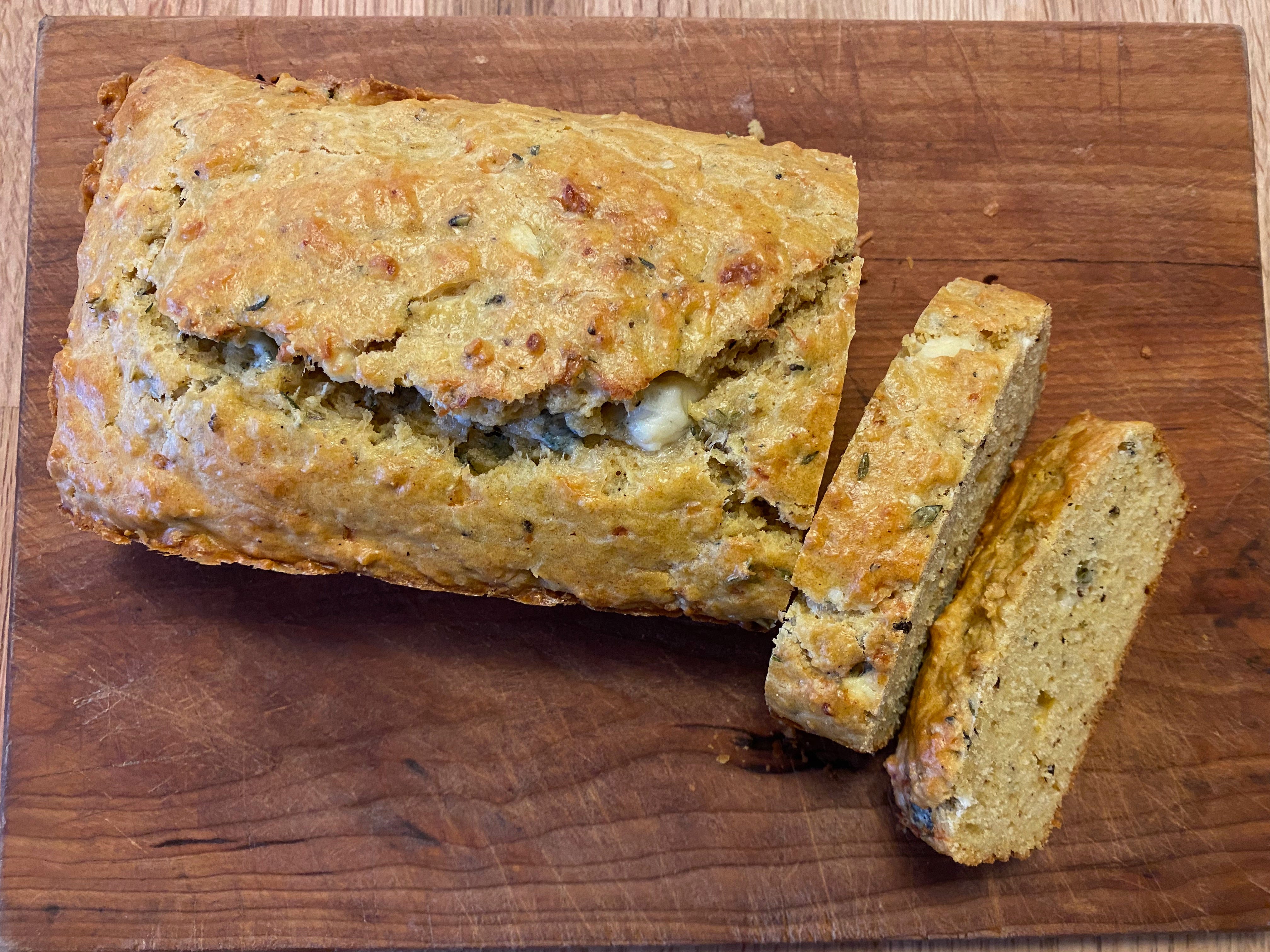 A rectangular loaf of bread with a crack along the top sits on a cutting board, next to a few already-sliced pieces.