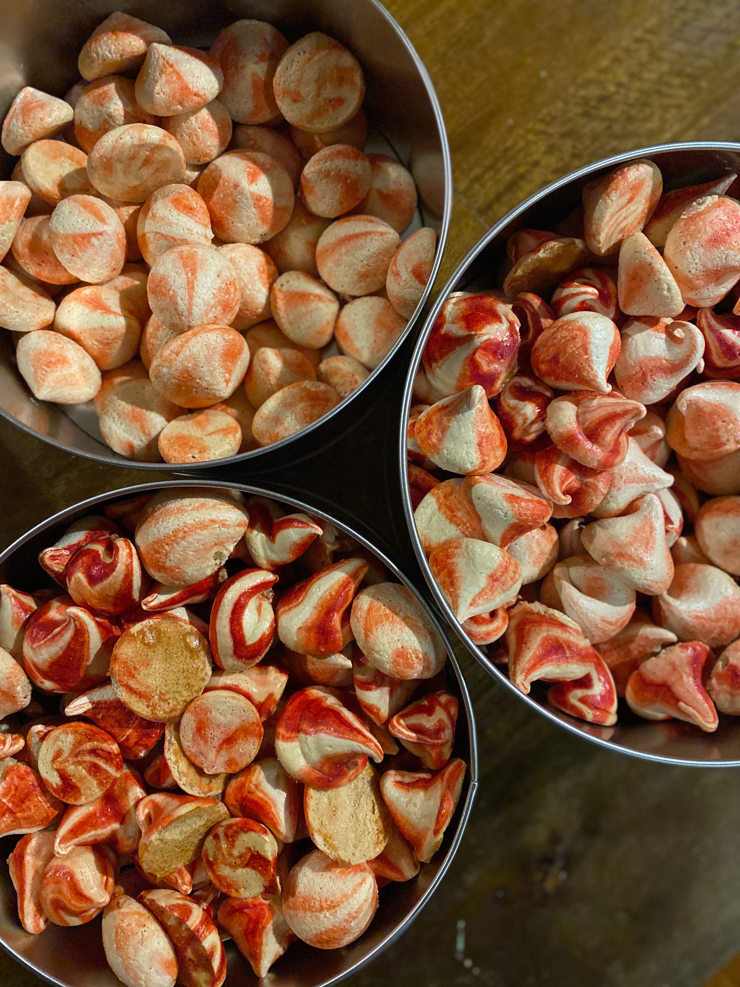 Three round silver tins full of small, teardrop-shaped, red and white swirled meringues.