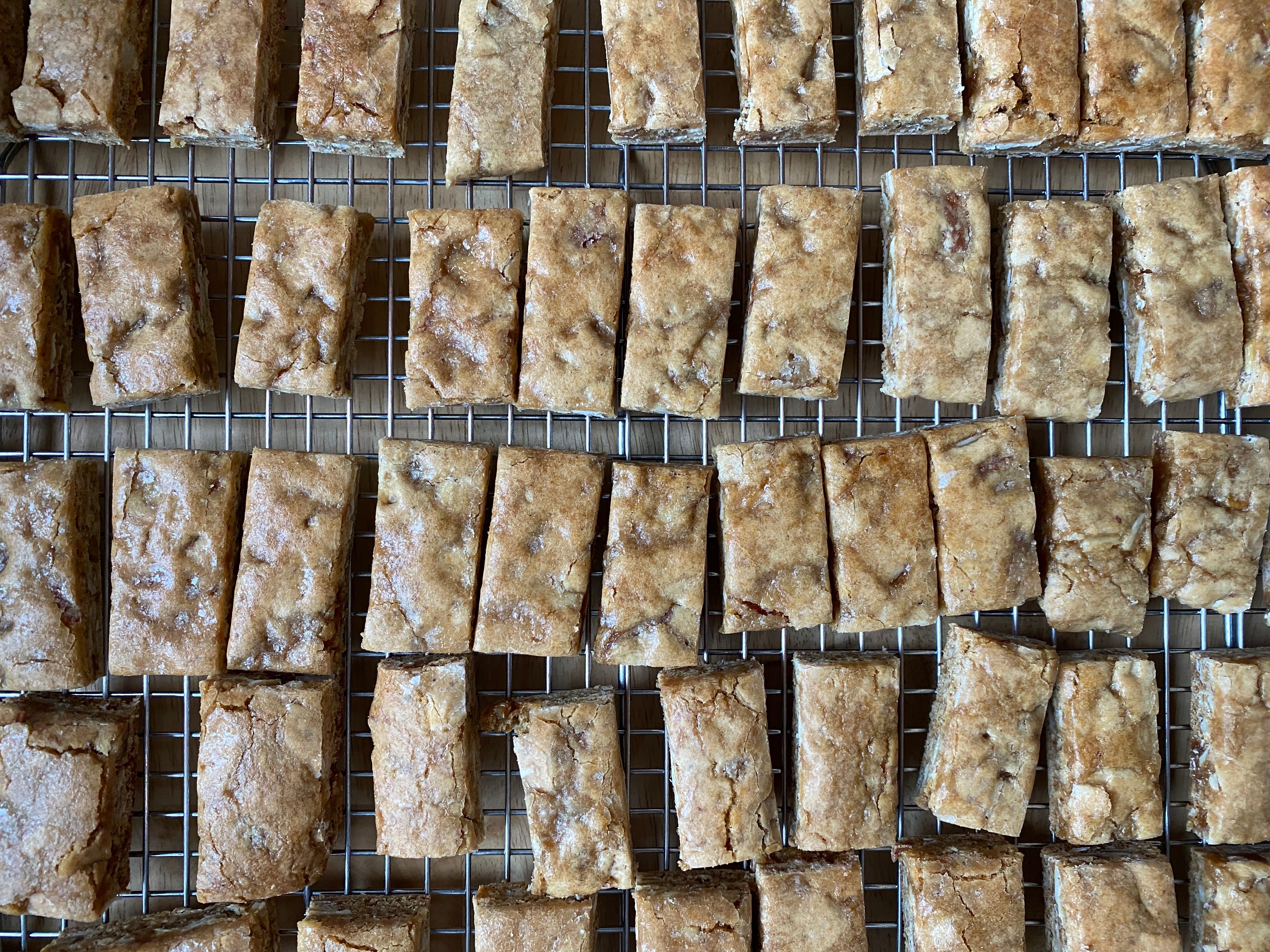 Many rows of small rectangular bars on a metal cooling rack. They’re golden brown, with little cracks and dimples on their tops, and a shiny glaze.