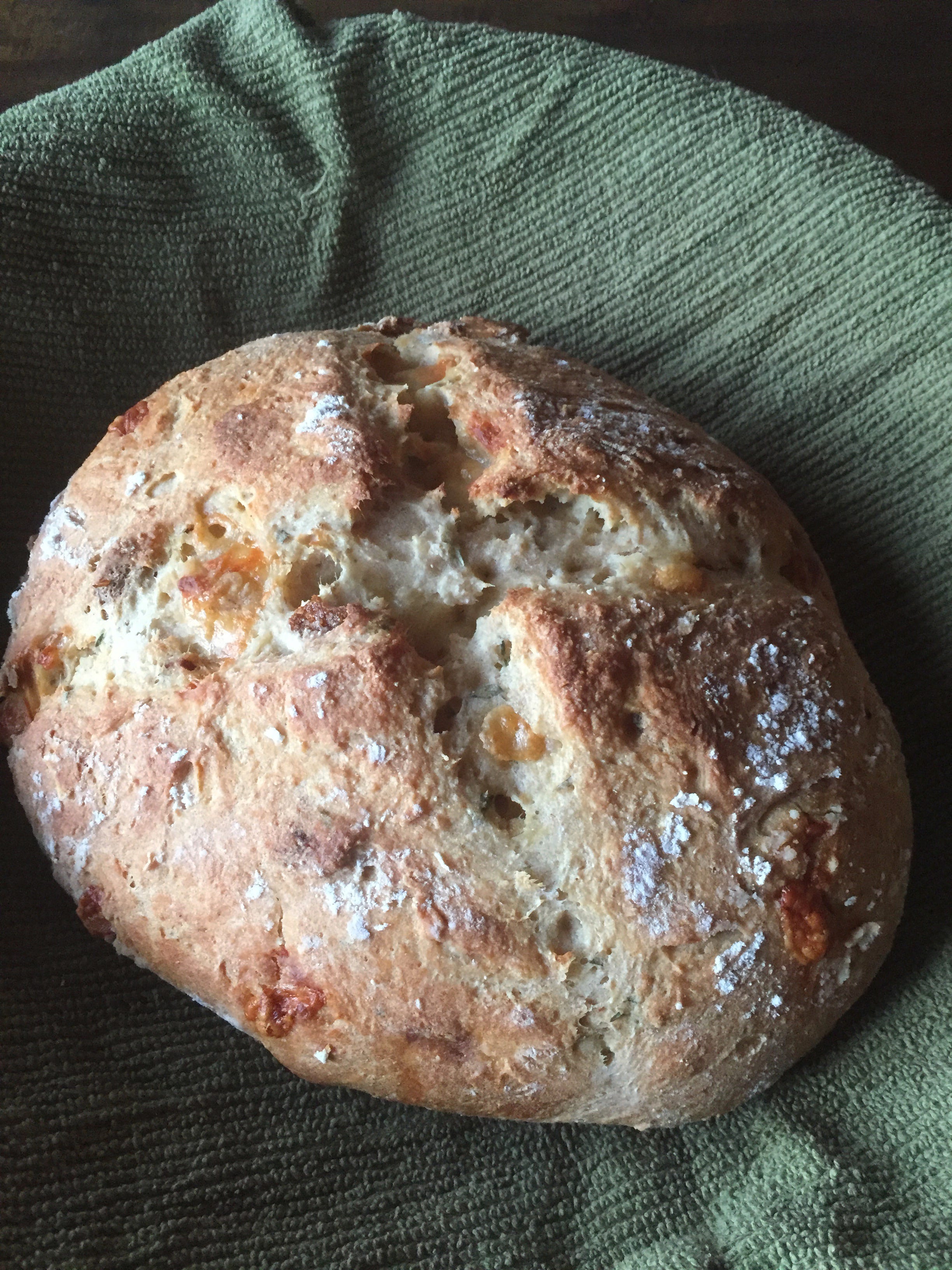 A loaf of golden brown soda bread sits in a basket lined with a green cloth.