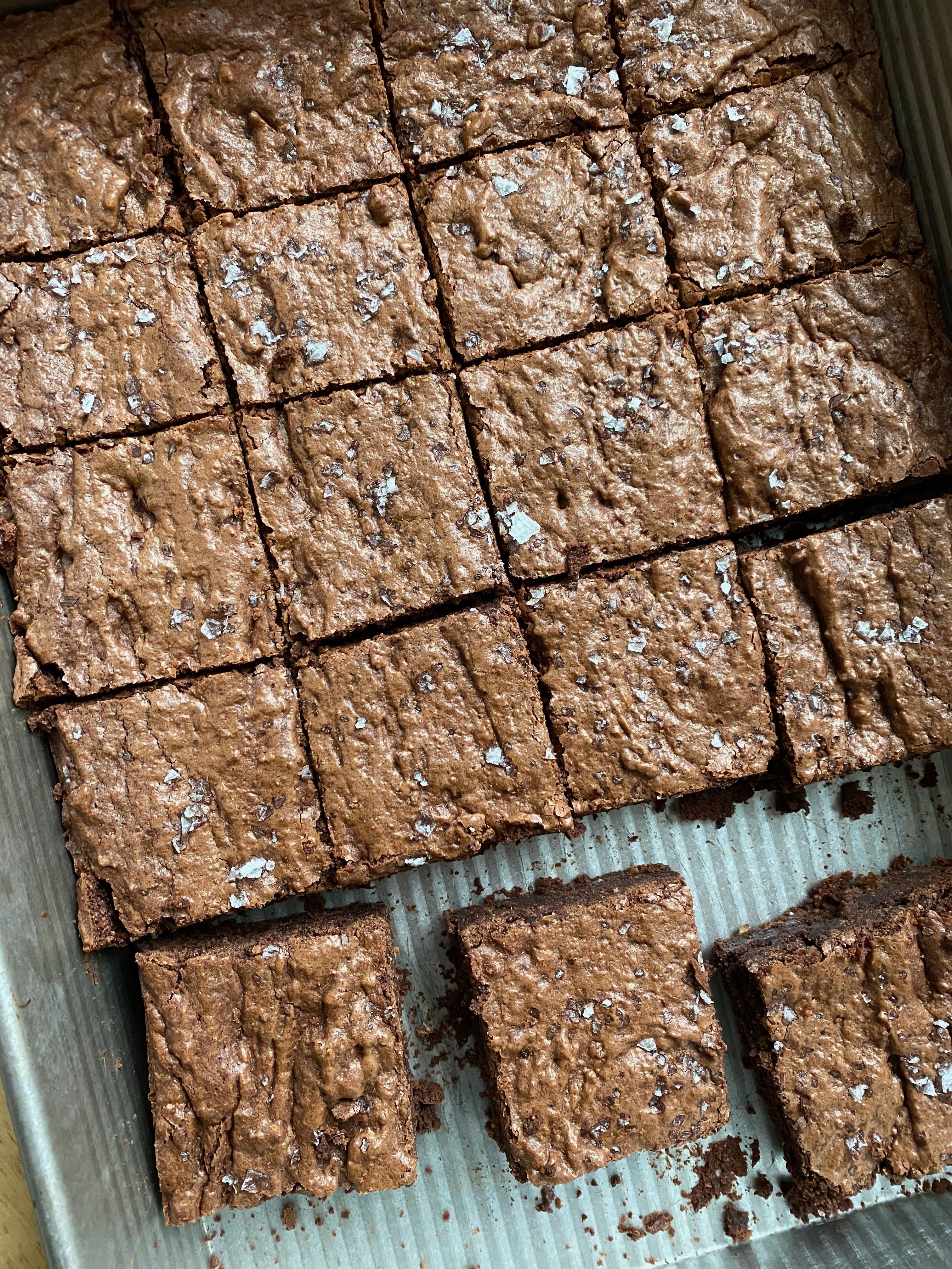 A pan of brownies sitting snuggly in a silver baking pan, with a few separated from the rest in the bottom of the photo.