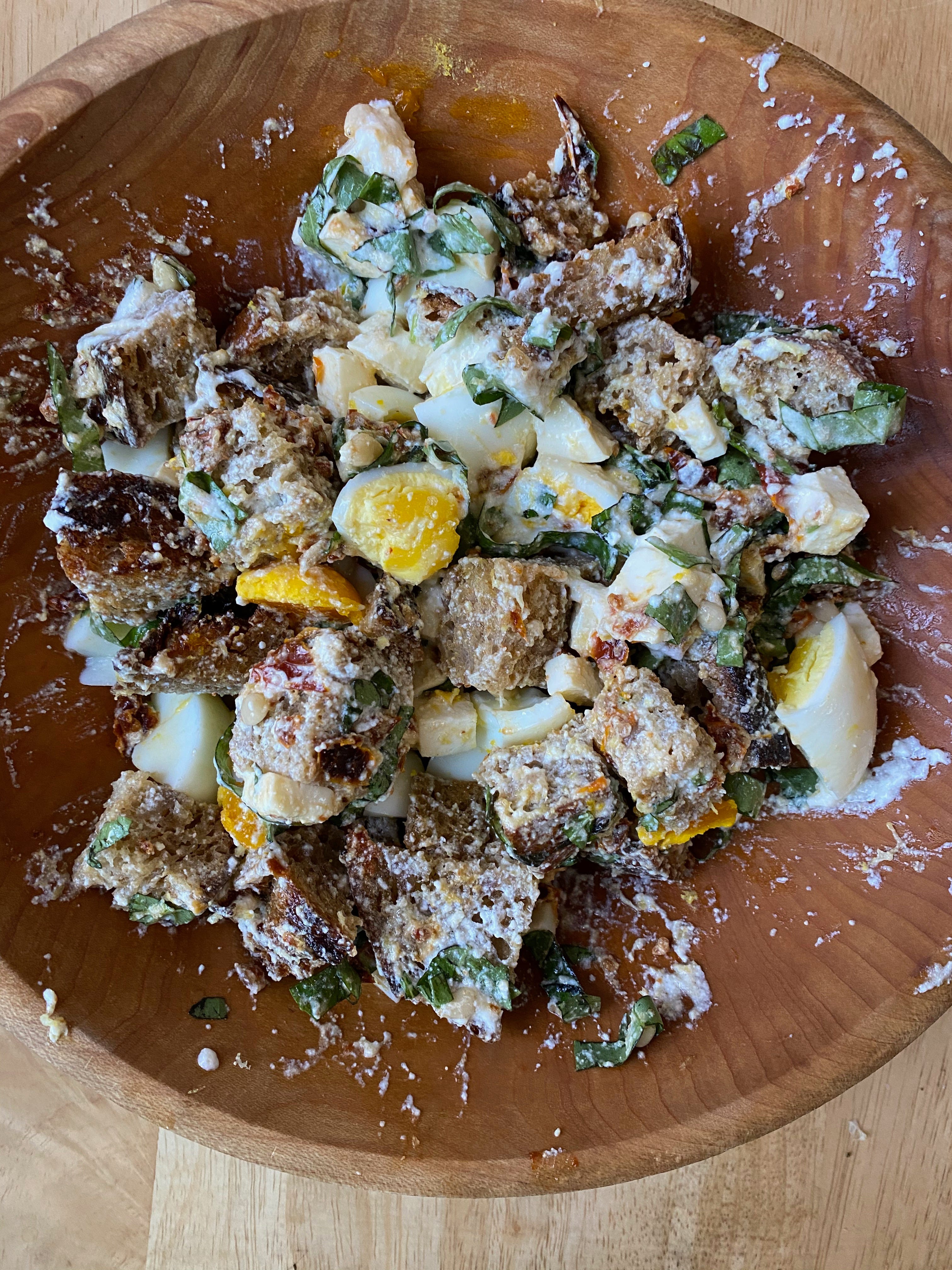A closeup of this panzanella in a wooden bowl: chunks of bread, hard-boiled eggs, and shredded basil, coated in ricotta cheese.