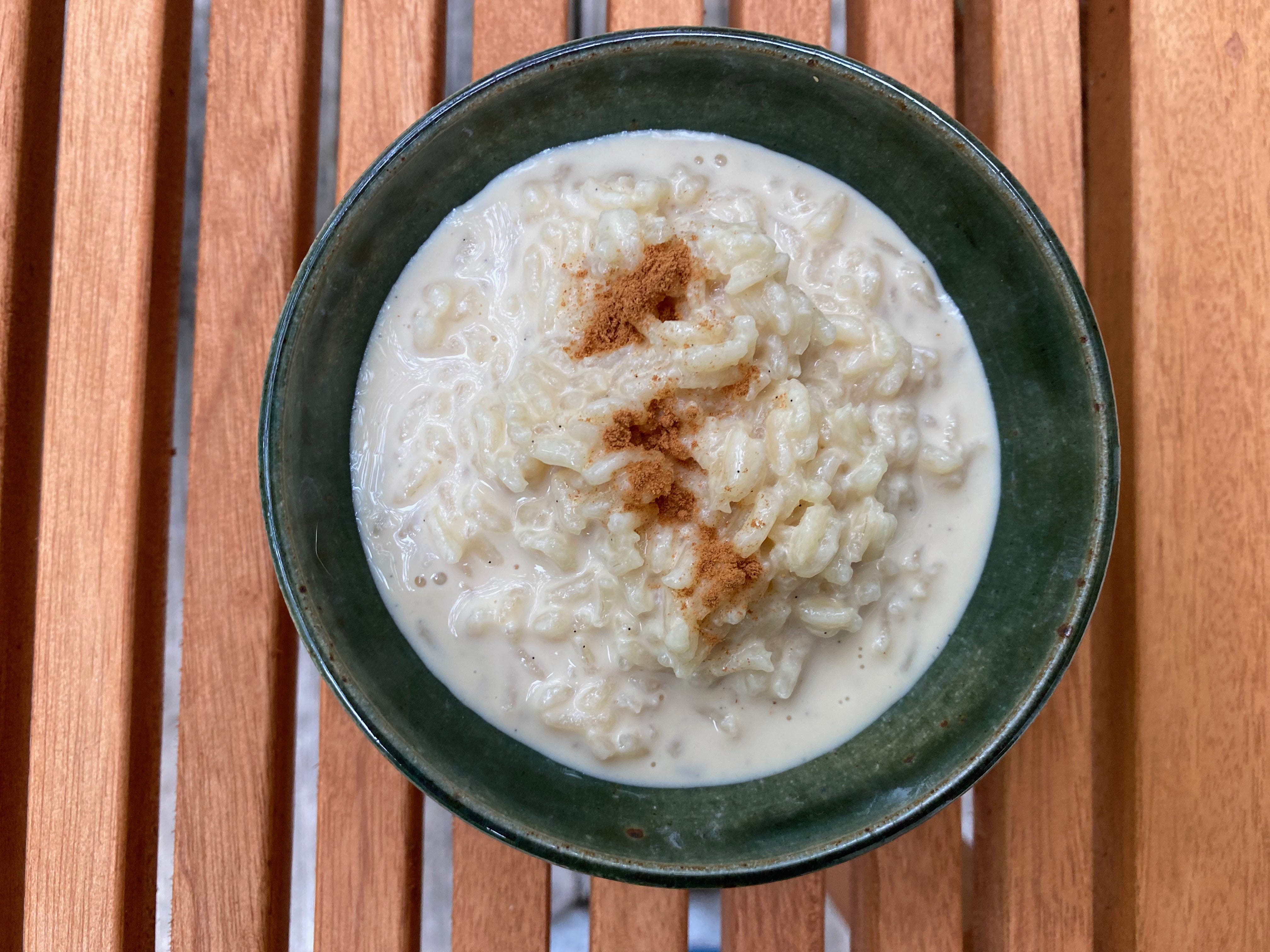 A small ceramic bowl of rice pudding sprinkled with cinnamon sits on a slated wooden coffee table.