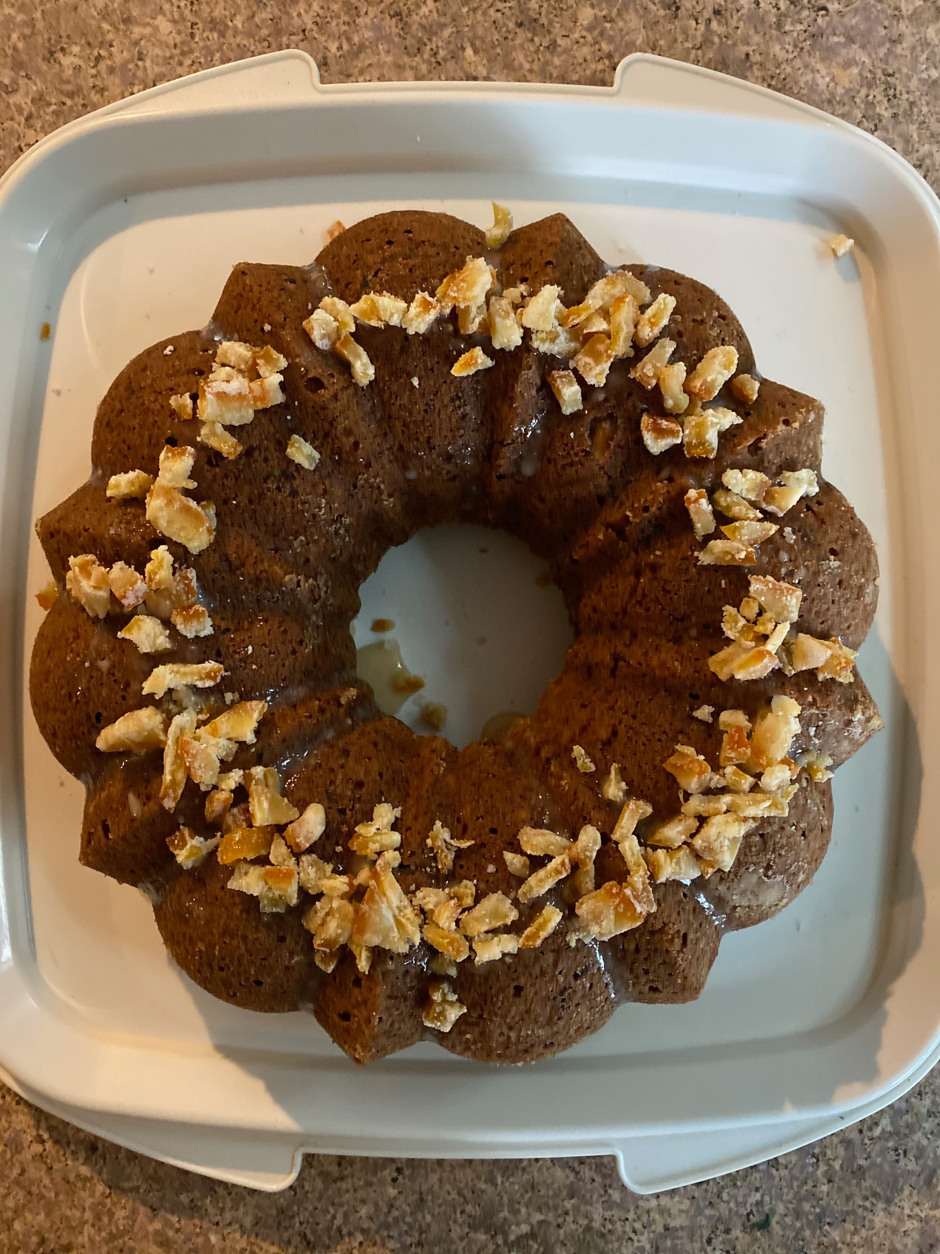 A round ring cake sits on a white plastic plate. It has fluted edges, and is decorated with copped candied orange.