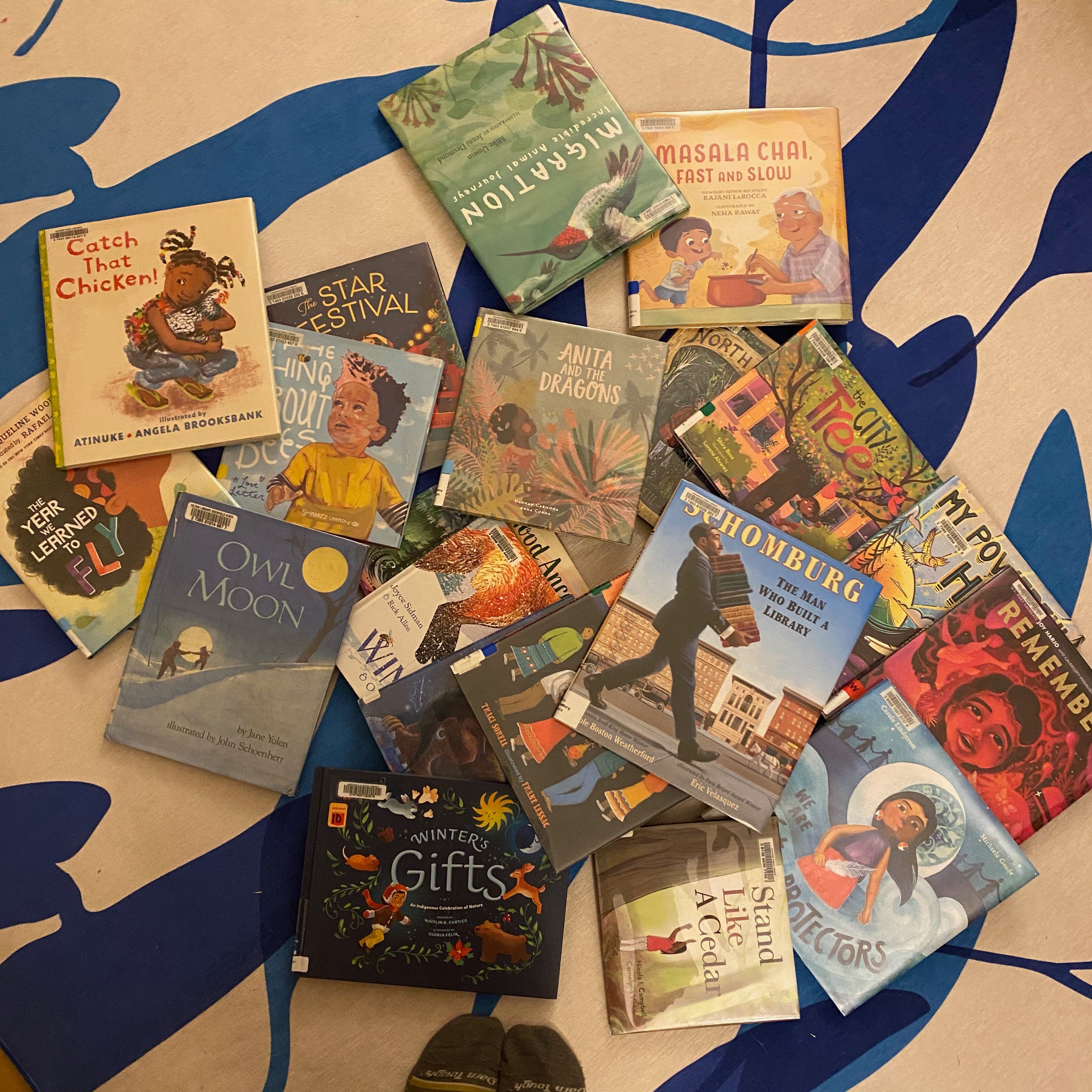 A big pile of picture books on a blue and white rug.