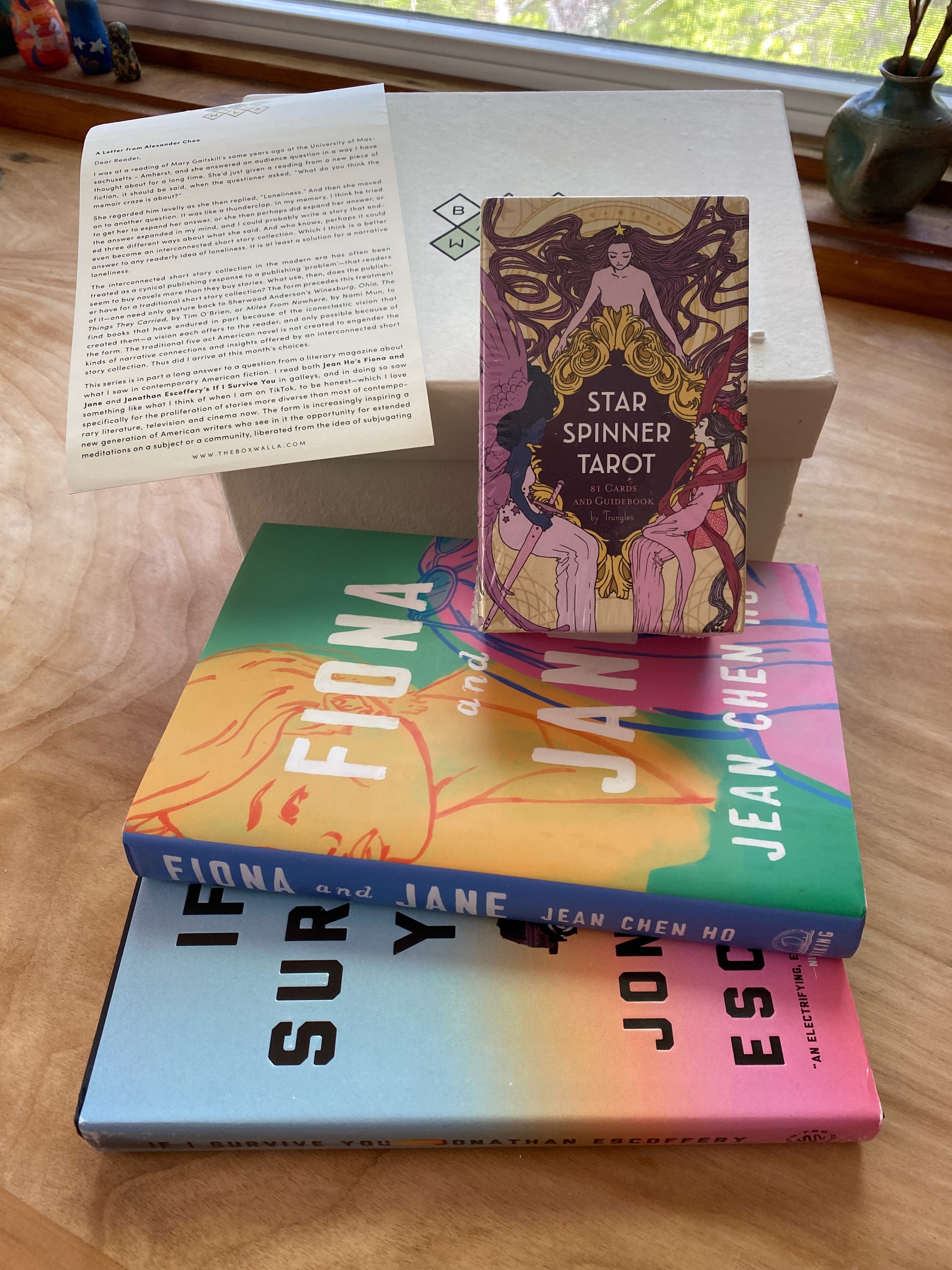 The two listed books, a box of tarot cards, a small typed letter, and a box with the Boxwalla logo arranged on a desk below a window.