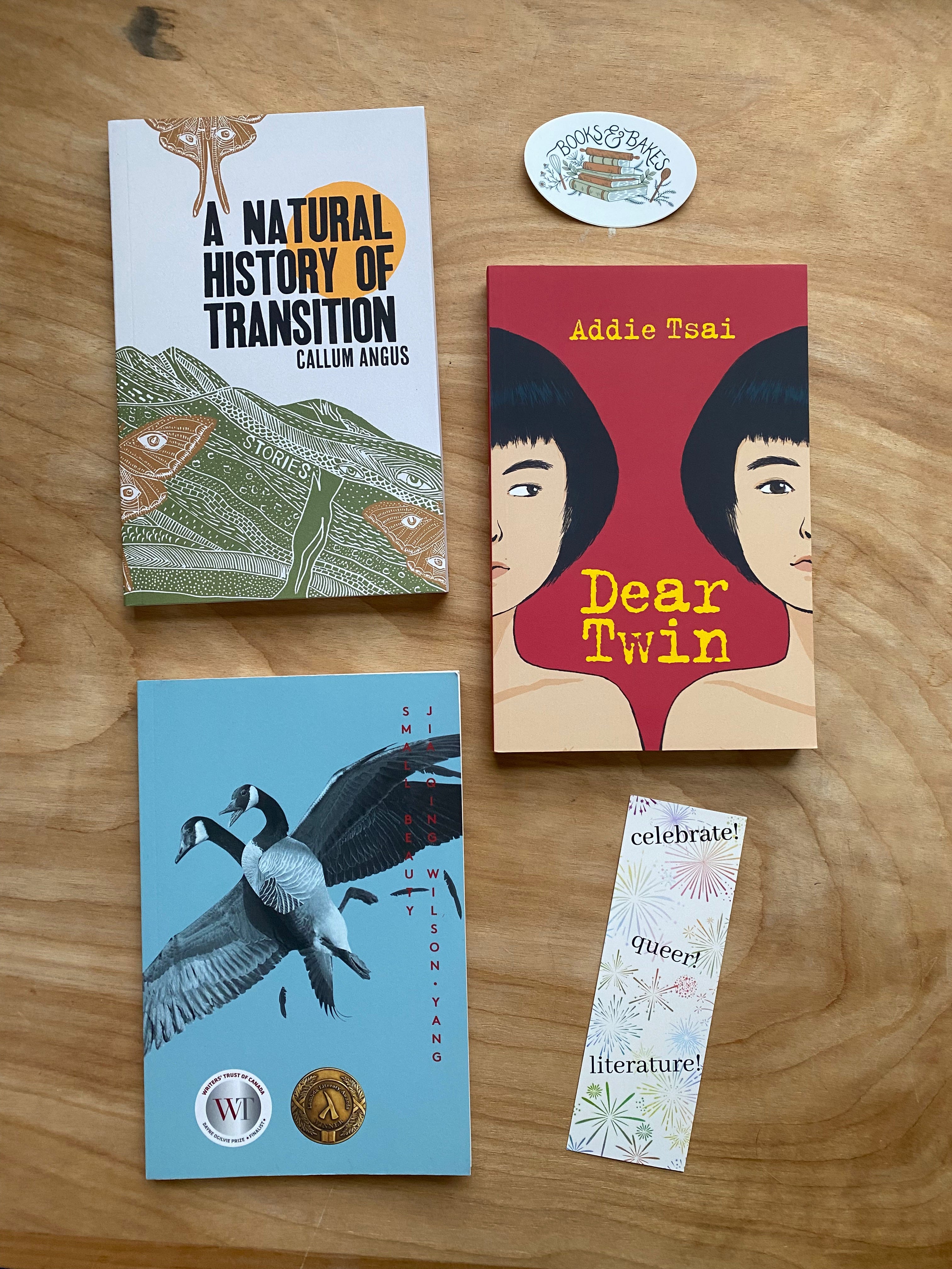 The three books mentioned arranged on a wooden desk next to a Books & Bakes sticker and bookmark.