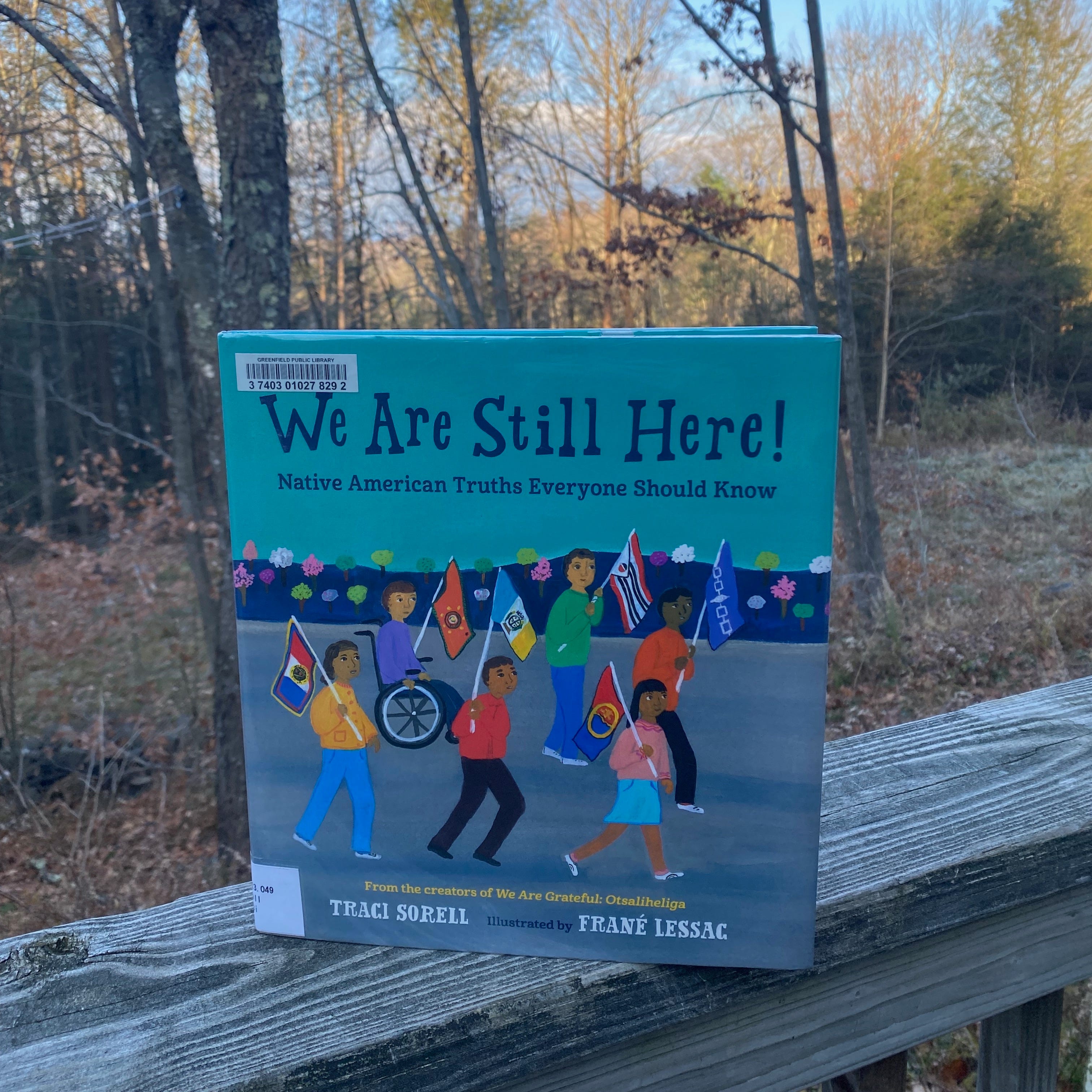 Pictured here standing on a porch railing in front of a sunlit winter forest. 