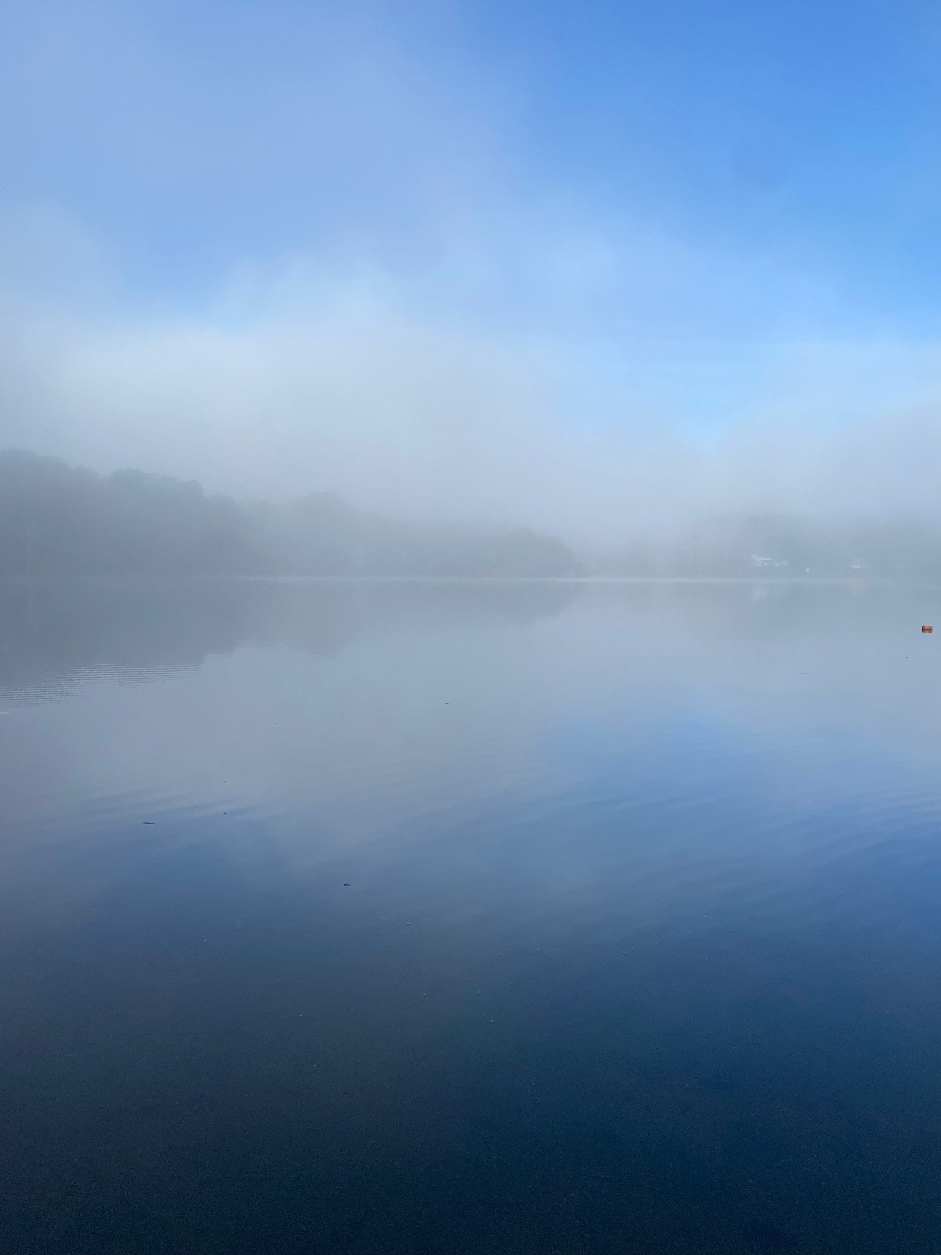 View of a misty lake; the water and line of hills on the horizon are vague and blurry behind the fog.
