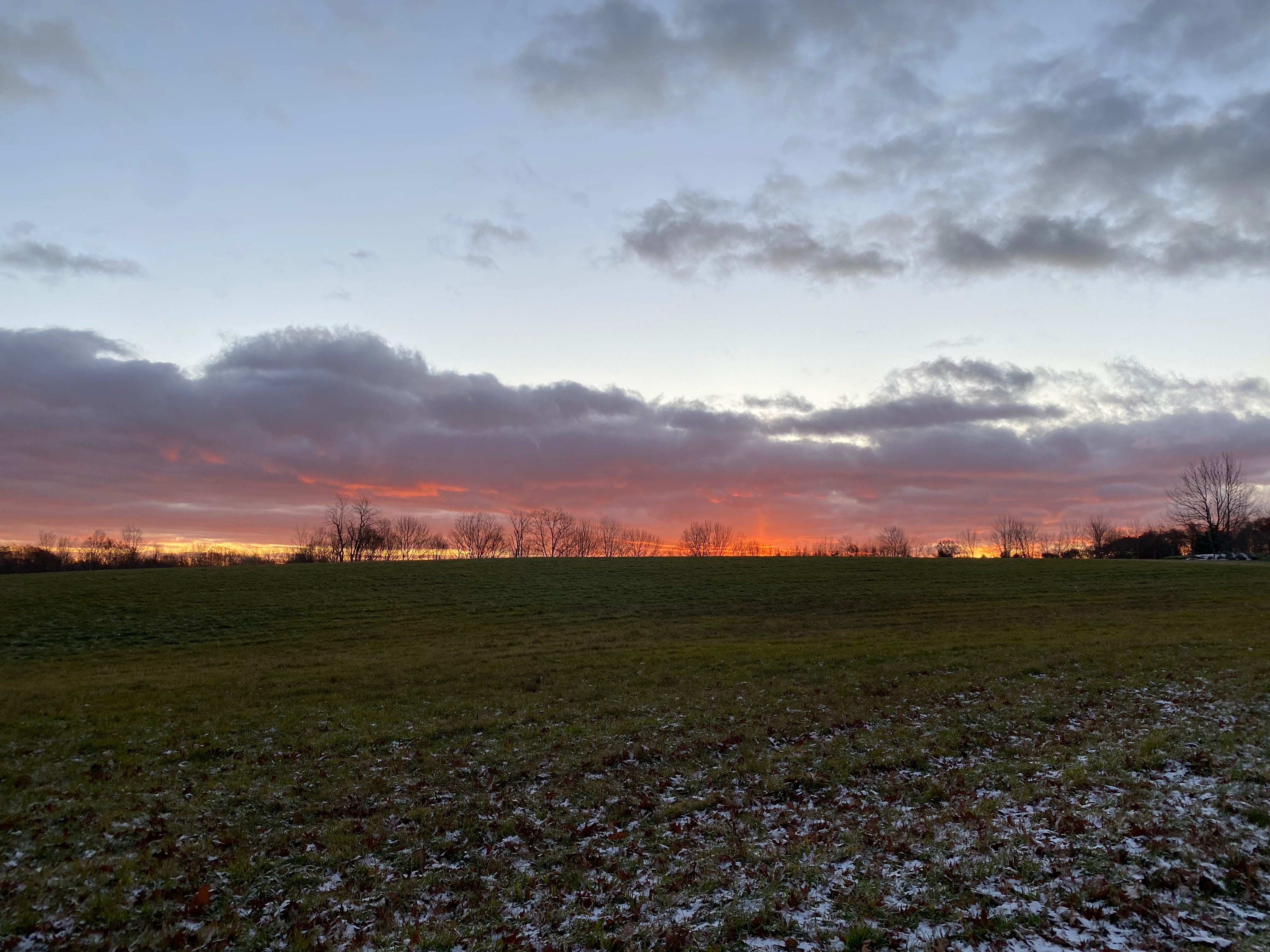 Sunrise vista over a green field dusted with snow.