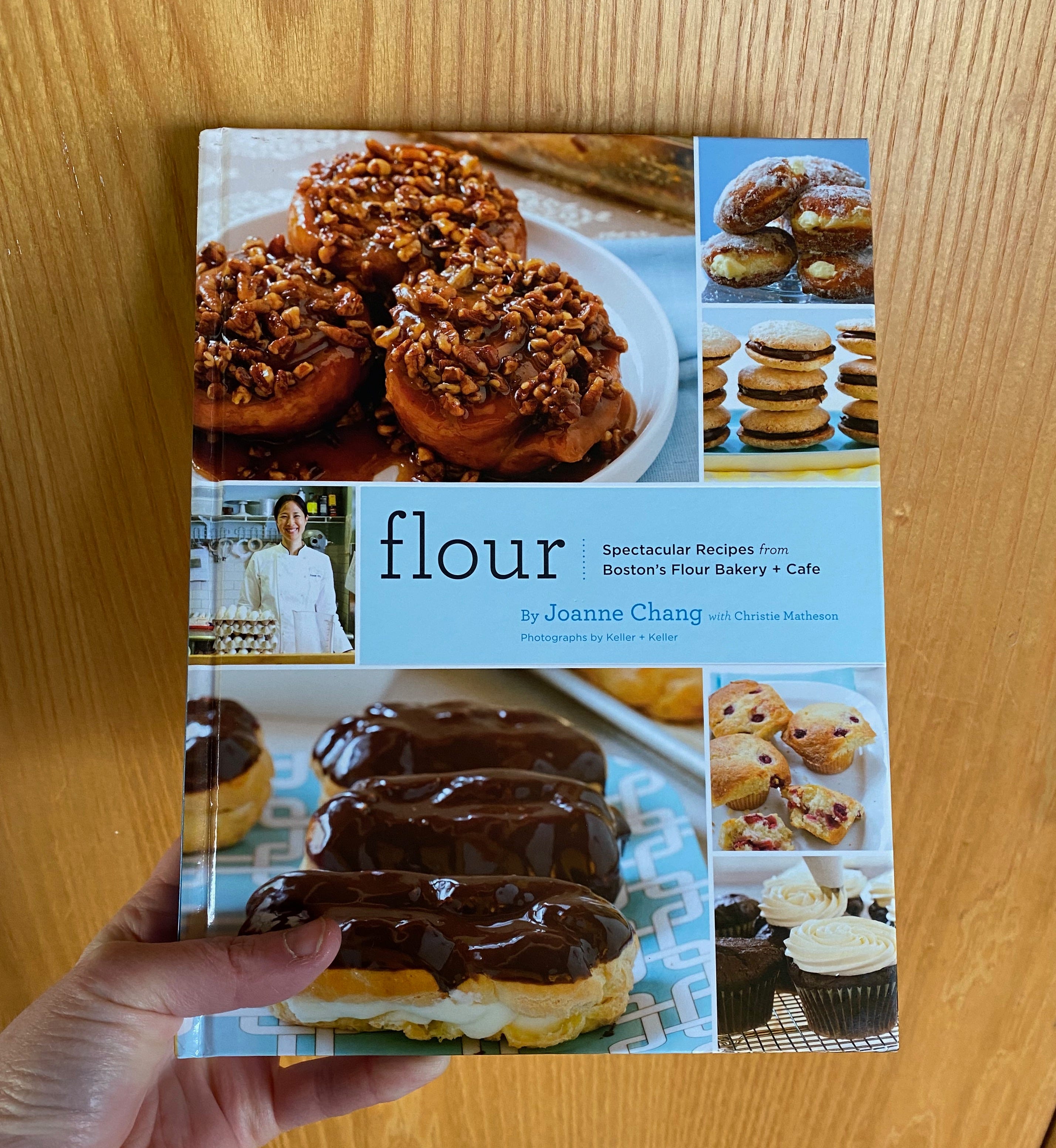My hand holding up Flour in front of a wooden cabinet door.