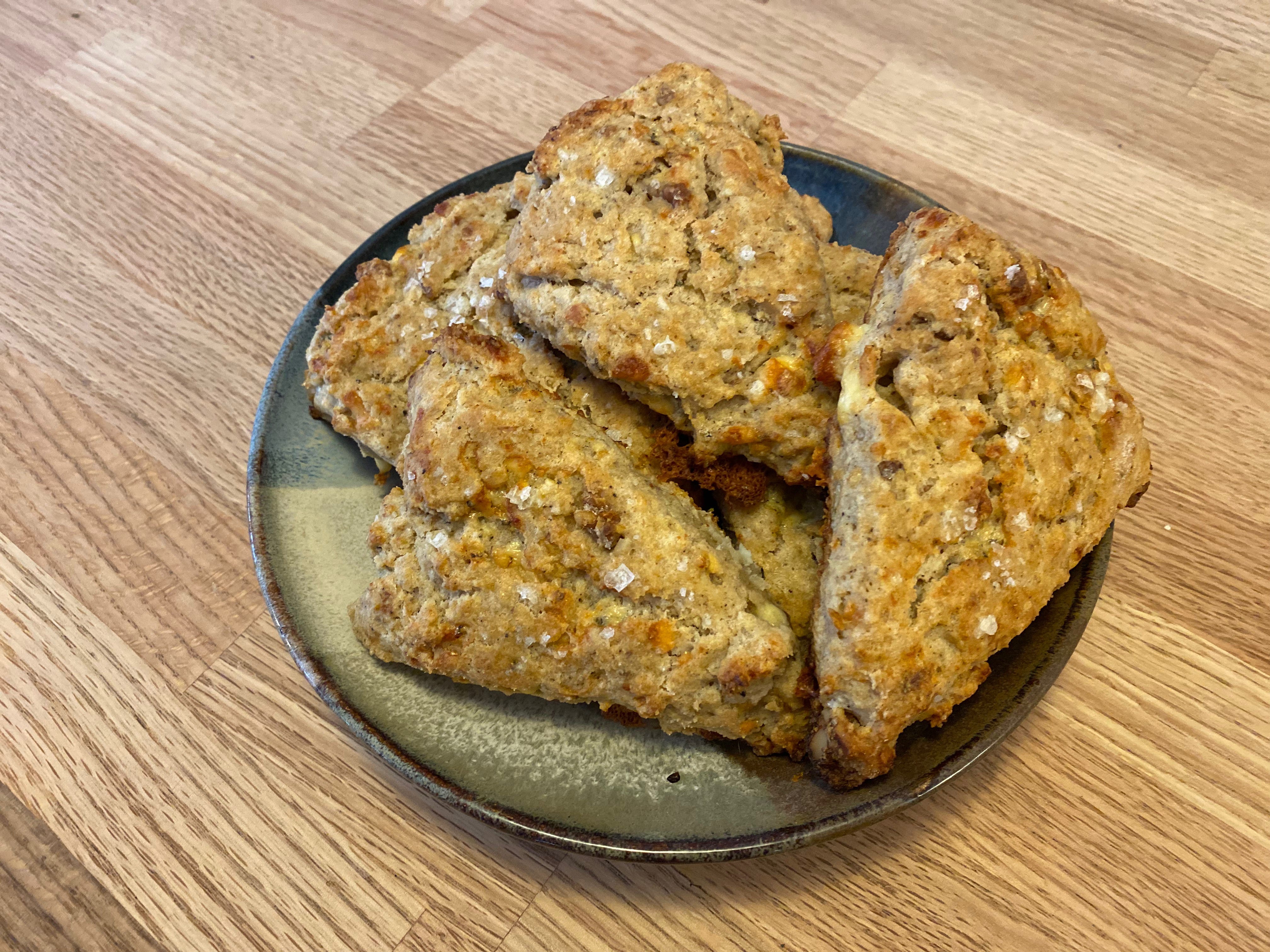 A plate of triangular scones dotted with flaky sea salt on a wooden counter.